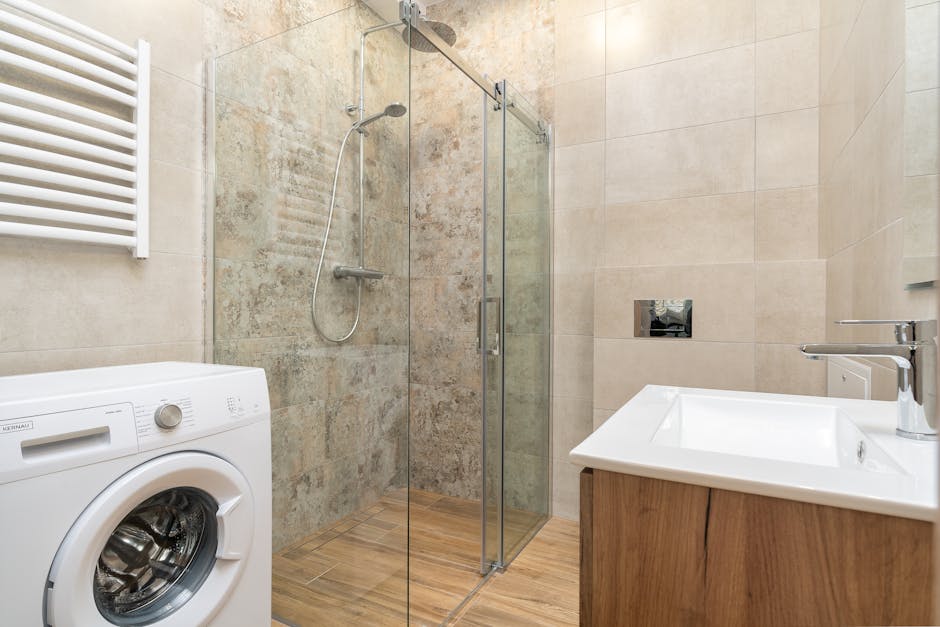 Elegancka łazienka z przeszkloną kabiną prysznicową, pralką i nowoczesną umywalką.